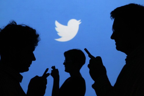 Personas sosteniendo teléfonos móviles silueteadas contra un fondo proyectado con el logo de Twitter en Varsovia